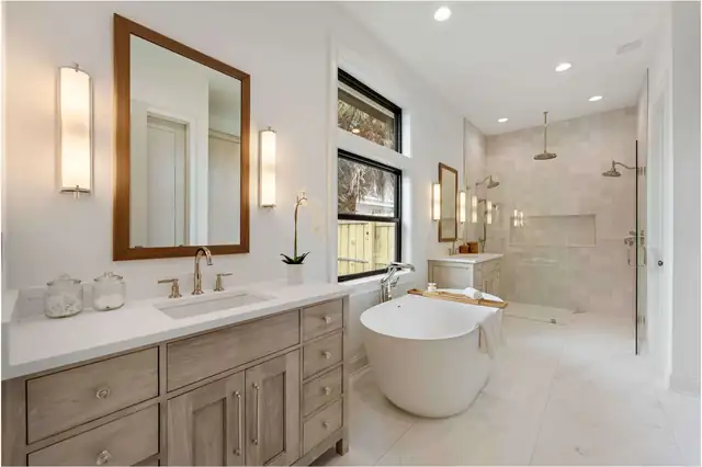Bright primary bathroom with light wood vanities, white countertops, a freestanding tub and a glass walk-in shower