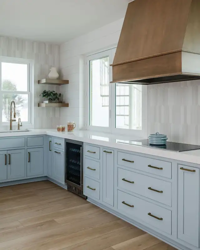Ponte Vedra kitchen with light blue cabinets, brass pulls, a wood range hood and white tile walls