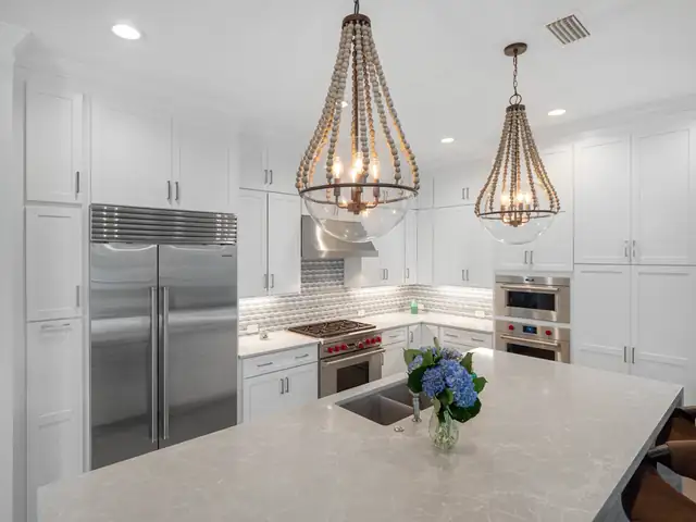 White shaker kitchen with a marble-look quartz island, stainless appliances and beaded globe pendant lights