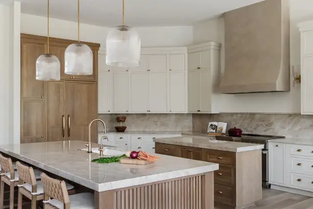 Coastal Oaks kitchen with cream and wood cabinetry, a large quartz island, glass pendants and a beige range hood