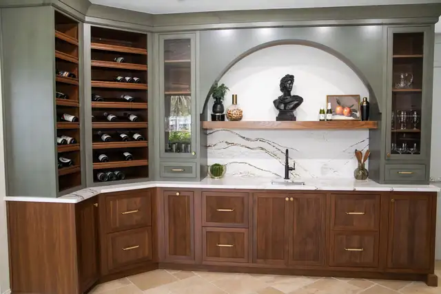 Custom wet bar with walnut base cabinets, sage green wine storage towers and an arched quartz backsplash